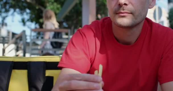 Человек ест картошку фри и вытирает рот в кафе на открытом воздухе — стоковое видео