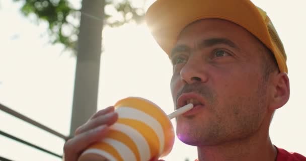 Mann mit Mütze genießt an sonnigem Tag Drink gegen Baumsilhouette — Stockvideo