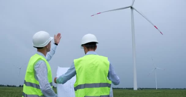 Engenheiros em capacetes discutem projeto de papel de turbina eólica — Vídeo de Stock