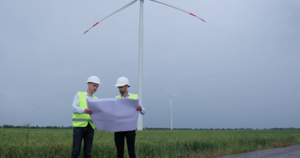 Engineers look at project sheet and point to wind turbine — Stock Video