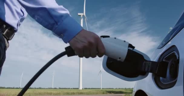 Homem insere ficha de carregamento para carregar carro elétrico pelo moinho de vento — Vídeo de Stock