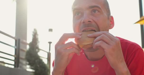 Positiv man biter hamburgare på uteservering — Stockvideo