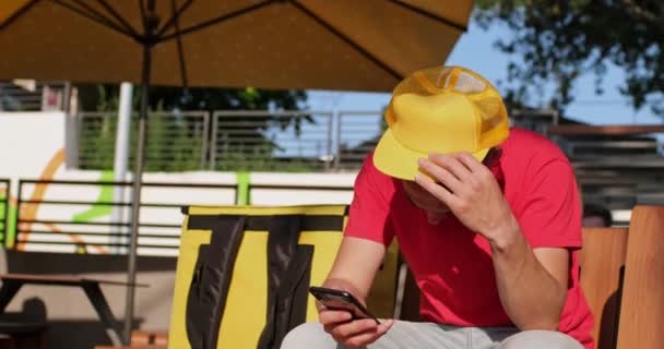 Kurýr s mobilním telefonem nastavuje čepici čekající na objednávku v kavárně — Stock video