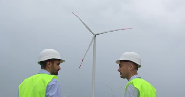 Ingenjörer diskuterar vindkraftverk som genererar energi på gården — Stockvideo