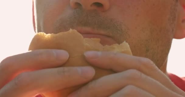 Hombre hambriento come hamburguesa fresca en primer plano día soleado — Vídeo de stock