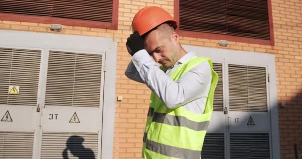 Arbeidstaker setter på oransje hjelm stående ved elektriske transformatorstasjoner – stockvideo