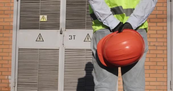 Werknemer houdt hardhat stand by substation op zonnige dag — Stockvideo