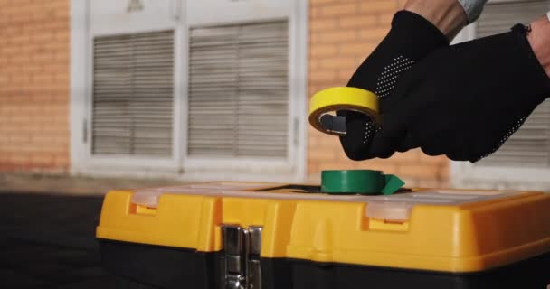 Muž rozmotává žlutou lepicí pásku přes skříňku s nářadím na rozvodně — Stock video