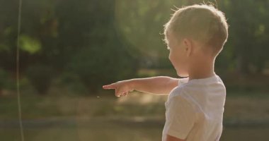 Anaokulu öğrencisi çocuk hevesle su üzerinde hareket eden gölgeyi işaret ediyor. Meraklı sarışın çocuk, hızlı hareket ettiğini fark ettiği anda küçük parmağını dalgalanan suya doğrultur.