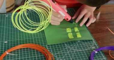 Çocuk, iş yerinde üç boyutlu kalemle sarı plastiğin dikdörtgen detaylarını yazıyor. Ortaokul öğrencisi okuldaki tasarım sınıfında oyuncakların parçalarını yapıyor. Çocuklar için bilim