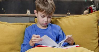 Odaklanmış okul çocuğu, sarı kanepe yastıklarının arasında oturmuş ders kitaplarının sayfalarını çeviriyor. Küçük çocuk masal okur. Oturma odasında vakit geçirir. Evde öğrenim