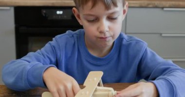 Ortaokul öğrencisi pervane takıyor ve masa başında tahta uçakla oynuyor. Küçük çocuk evde toplanan kontrplak detaylarının oyuncak uçak modelini bitirmekten mutlu.