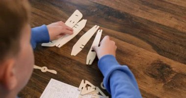 Çocuk okul çocuğu masa başında toplanmak için ahşap uçak detaylarını ayarlar. Akıllı çocuk evde klasik uçak modeli yapmaya hazırlanıyor.