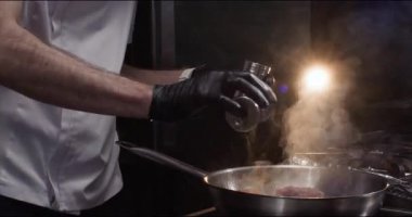 Şef, et filetoya baharat ekliyor. Mutfaktaki tavada yakın plan. Usta, süslü restoranlarda dana etinin daha lezzetli olması için baharat kullanır. Akşam yemeği hazırlığı