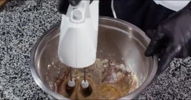 Şef, metal kasede pasta hamuru yapmak için güçlü mikser kullanıyor. Baker, restoran mutfağında yumurta kakao tozu ve şekerle lezzetli turtalar pişiriyor. Tatlı.