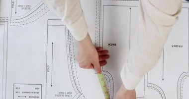 Terzi, desen parçalarının tam boyutlarını ölçmek için mezura kullanıyor. Kadın, doğru kıyafet üretimi için desen bileşenlerinin şeklini ve boyutunu izler.