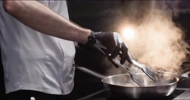 Eldiven ustası mutfaktaki et dilimlerini maşayla kızartma tavasına çeviriyor. Yetenekli şef şık restoranlarda et yemeği pişirir. Profesyonel yemek hazırlama.