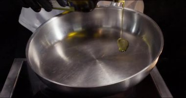 Şefin elleri mutfaktaki sıcak paslanmaz kızartma tavasına zeytinyağı döküyor. Eldivenli adam restoranda lezzetli yemekler pişirmek için sıvı yağ ekler. Lezzetli yemek malzemesi