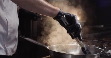 Şefin elleri paslanmaz kızartma tavasındaki malzemelerle mutfak maşasını birbirine karıştırır. Usta restoranda ocakta yemek pişirmeyi bitirir. Yemek tarifleri