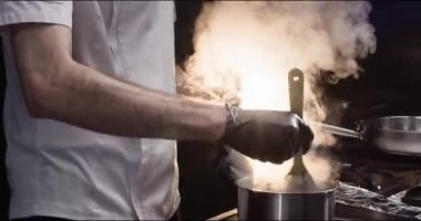 Şef, hızlı yemeği paslanmaz tencereyle mutfak kapağında tahta kürekle karıştırıyor. Efendi lokantada artan buharla sıcak yemek pişiriyor. Yemek takımı ve soba kullanımı