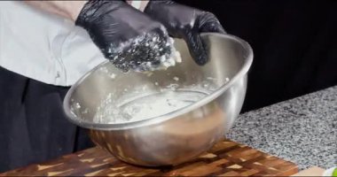 Siyah eldivenli şef metal kasede güçlü hamur yoğurur. Baker, taş mutfak tezgahında sağlıklı malzemelerden oluşan turta pişirir. Fırın çalışanı