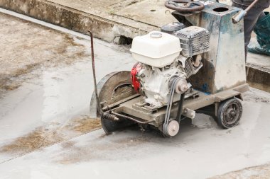 İnşaat alanında beton yol kesen elmas testeresi kullanan bir işçi.