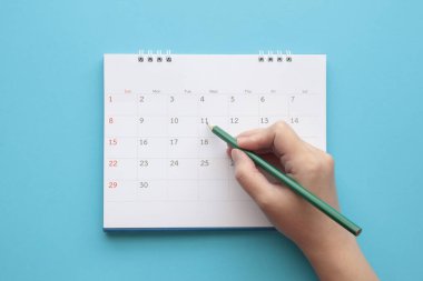 Mavi arkaplanda takvim tarihi üzerinde kalem izi olan el