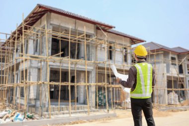 İnşaat şantiyesindeki koruyucu miğfer ve planlar üzerinde çalışan genç profesyonel mühendis.