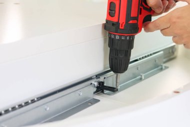 Beyaz masa mobilyalarını kablosuz tornavida kullanarak evde monte eden adam.