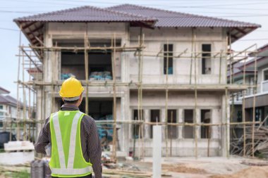 İnşaat şantiyesindeki koruyucu miğfer ve planlar üzerinde çalışan genç profesyonel mühendis.