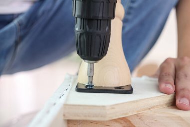 Adam evde kablosuz tornavida kullanarak mobilya monte ediyor.