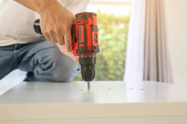 Beyaz masa mobilyalarını kablosuz tornavida kullanarak evde monte eden adam.