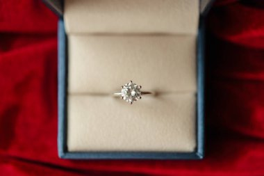 Kırmızı kumaş arka planda mücevher hediye kutusunda elmas yüzük.