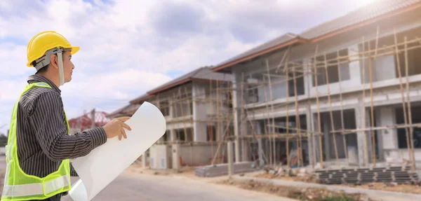 young professional engineer in protective helmet and blueprints paper at the house building construction site