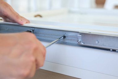 Asyalı adam beyaz masa mobilyalarını evde monte ediyor.