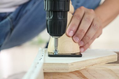 Adam evde kablosuz tornavida kullanarak mobilya monte ediyor.