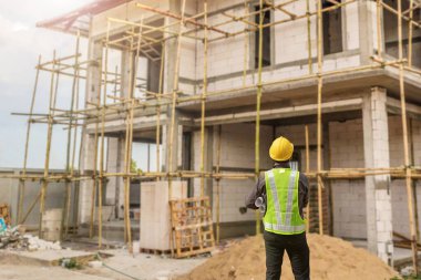 İnşaat şantiyesindeki koruyucu miğfer ve planlar üzerinde çalışan genç profesyonel mühendis.