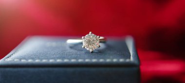 Kırmızı kumaş arka planında mücevher hediye kutusu olan elmas yüzük.