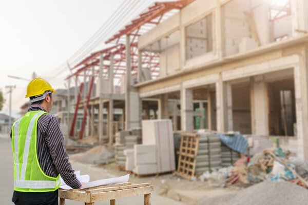 young professional engineer in protective helmet and blueprints paper at the house building construction site