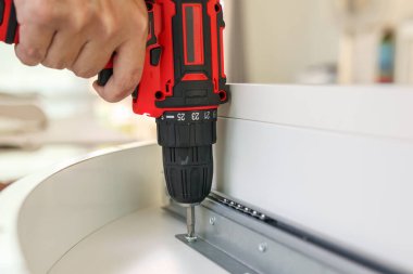 Beyaz masa mobilyalarını kablosuz tornavida kullanarak evde monte eden adam.