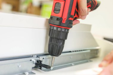 Beyaz masa mobilyalarını kablosuz tornavida kullanarak evde monte eden adam.