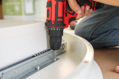 Beyaz masa mobilyalarını kablosuz tornavida kullanarak evde monte eden adam.