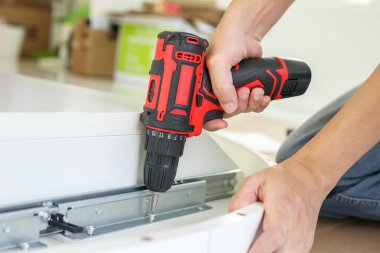 Beyaz masa mobilyalarını kablosuz tornavida kullanarak evde monte eden adam.