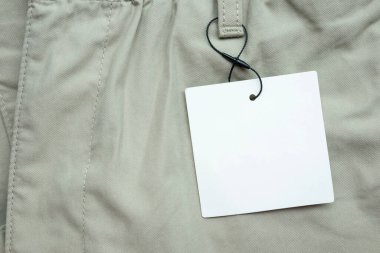 Gri kumaş doku arka planında boş beyaz kıyafet etiketi