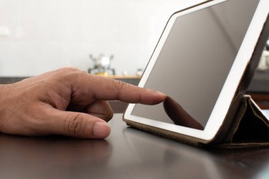 Yakın çekim, insanlar mutfakta yemek aramak için tablet kullanıyorlar. Yemek yapmayı öğrenmek için parmağı beyaz bir tablete dokunan bir adam. Boşluğu kopyala, bulanık arkaplan