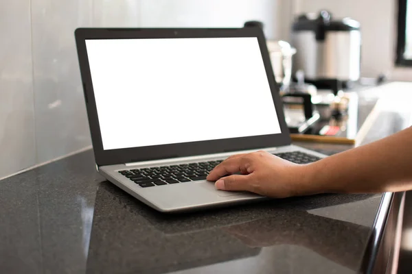 Closeup, A woman\'s hand is typing on a laptop keyboard to search out how to cook. notebook computer white screen on the table. Has a pot on the gas stove. Blurred background, moke up, clipping path