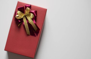 Kırmızı renk sunar kırmızı ve altın kurdeleli kutuyu sağ taraftaki kopyalama alanı olan beyaz bir masaya yerleştirir metin yazabilir, yakın çekim fotoğraf çekebilir ve üstteki görünüm manzara..