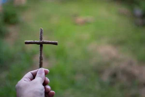 His left-hand holding a cross. right copyspace for entering text. Closeup photographing with background green and blurred.