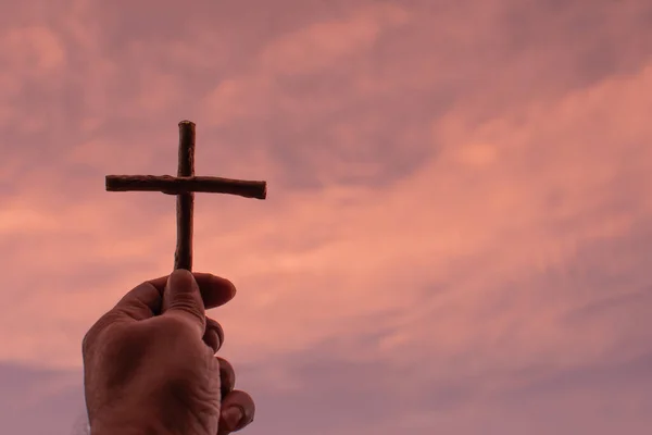 His left-hand holding cross up to the golden yellow sky. Left copyspace for entering text. Close-up shot with blurry clouds on a fine day.