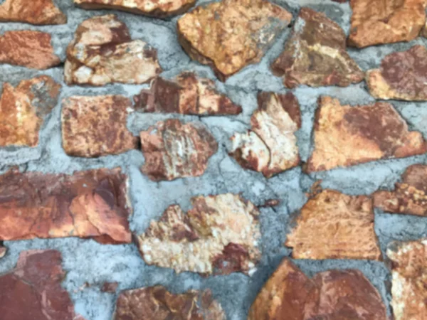 Close up and blurring of the old patterned stone wall and has cement to keep it strong. The rocks are stacked. The stones are brown, orange, gray, beautiful. Background landscape.